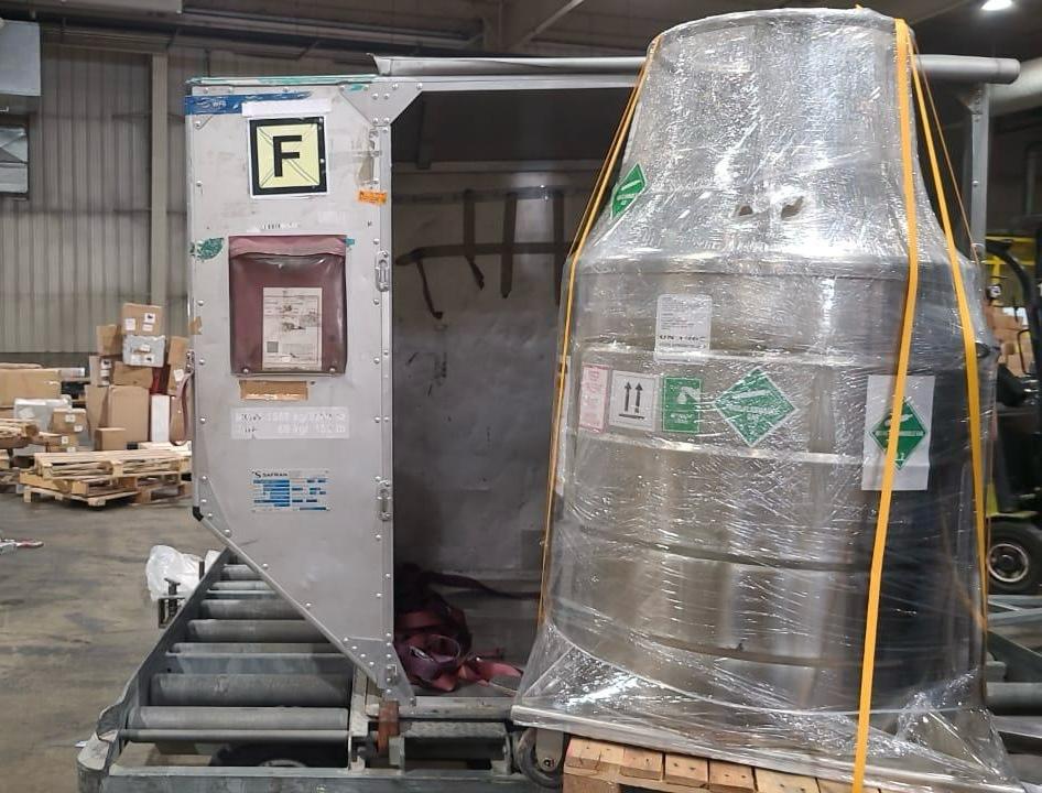 Liquid helium dewar wrapped and strapped to a pallet beside an air-freight container in a warehouse